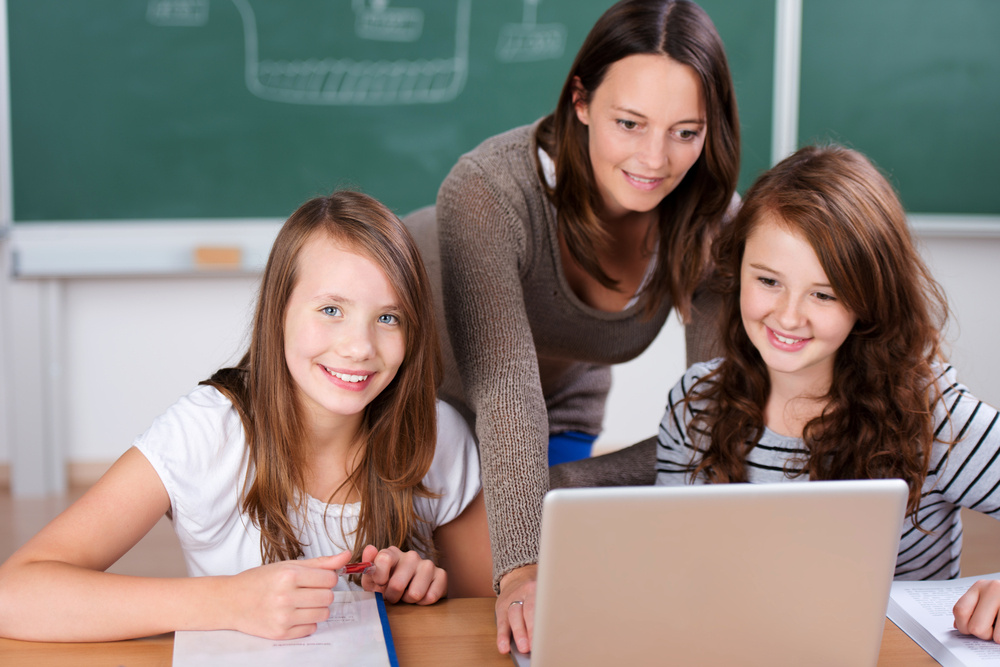 Cheerful teacher teaching her two students with laptop inside the classroom