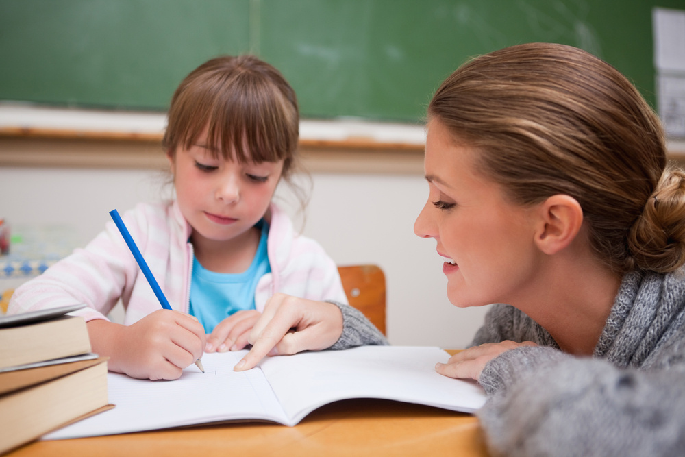 Cute schoolgirl writing a while her teacher is talking in a classroom