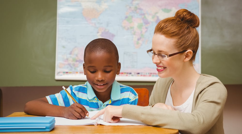 Portrait of teacher assisting little boy with homework in the classroom