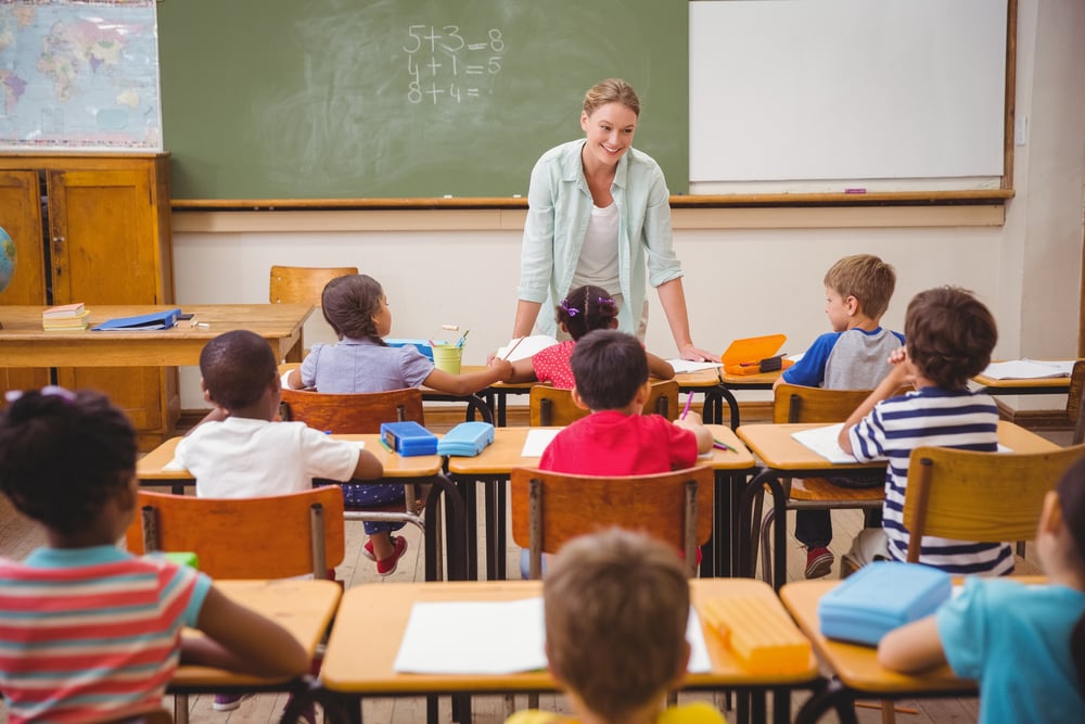 Pretty teacher talking to the young pupils in classroom at the elementary school