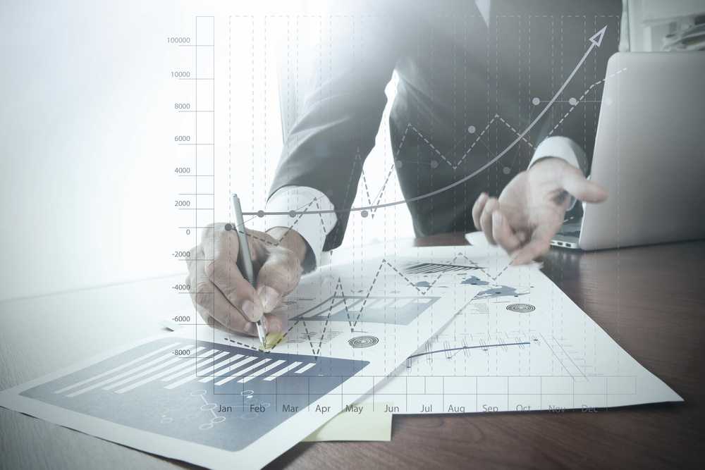 close up of businessman hand working on laptop computer with business graph information diagram on wooden desk as concept