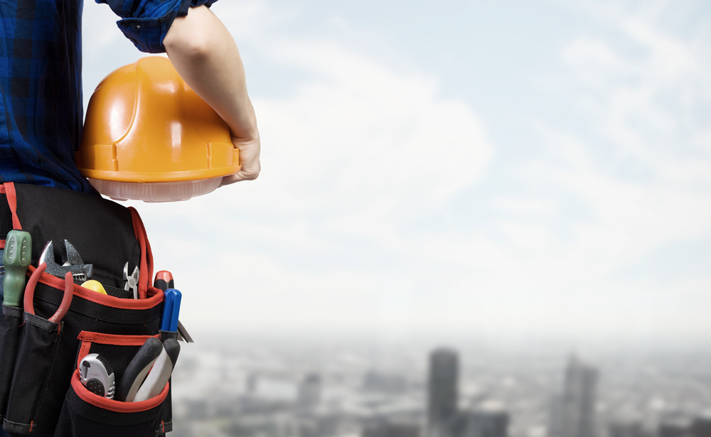 Close up of woman mechanic with yellow helmet in hand against city background